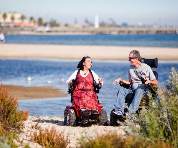 Fröhliches Paar mit Elektro-Rollstühlen am Strand
