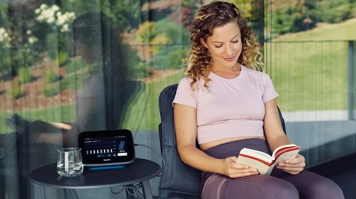 Eine Frau sitzt entspannt und liest, während das BEMER evo System neben ihr in Betrieb ist.