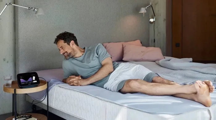 Ein Mann liegt entspannt im Bett, während das BEMER evo System neben ihm verwendet wird.