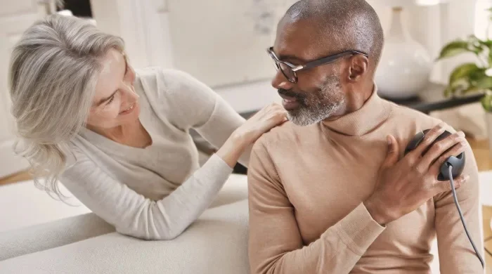 Ein Mann behandelt seine Schulter mit dem BEMER evo System, eine Frau unterstützt ihn dabei.