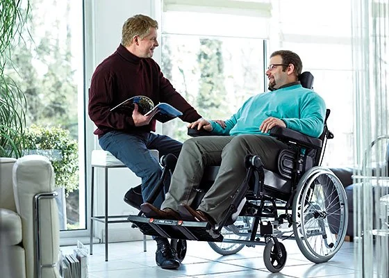 Beratungssituation mit Mann im Rollstuhl und Berater in hellem Raum.