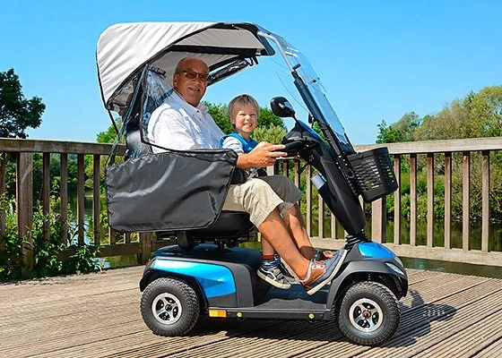 Senior fährt ein Elektromobil mit Wetterschutz, ein Kind sitzt mit auf dem Fahrzeug.