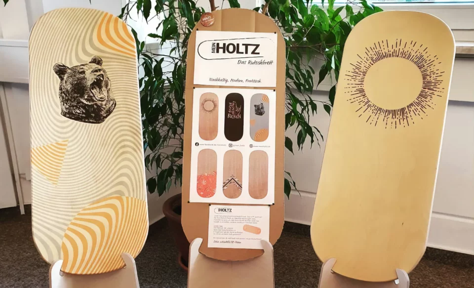 Drei hölzerne Rutschbretter mit Grafiken und Infoboard „meinHoltz Rutschbretter“.