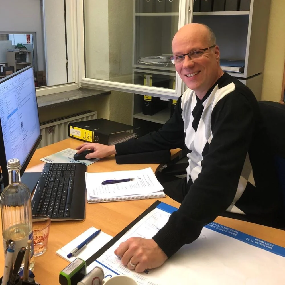 Olaf Thode sitzt lächelnd am Schreibtisch im Büro und arbeitet am Computer.