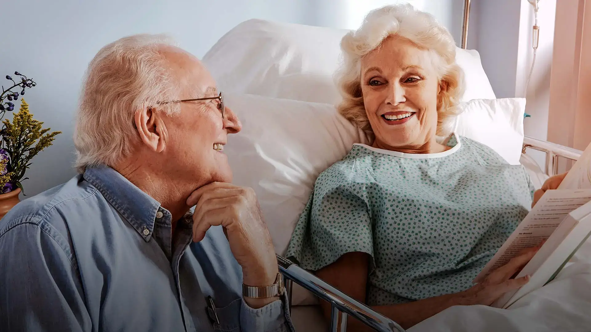 Älterer Mann sitzt am Bett seiner Frau